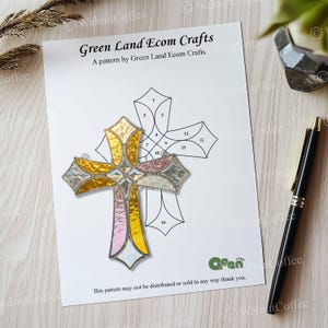 K&ouml;nnte beinhalten: Ein Buntglaskreuz mit goldenen, rosa und silbernen Abschnitten liegt auf einem wei&szlig;en Papier mit einer Kreuzzeichnung. Auf dem Papier steht "Green Land Ecom Crafts". Rechts liegt ein schwarzer Stift.