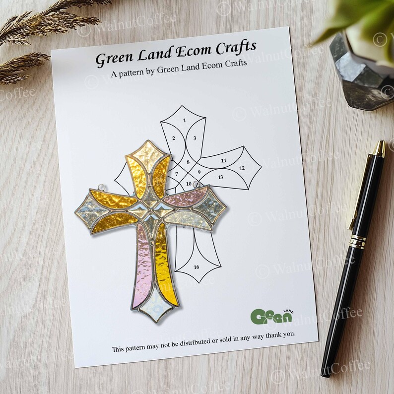 K&ouml;nnte beinhalten: Ein Buntglaskreuz mit goldenen, rosa und silbernen Abschnitten liegt auf einem wei&szlig;en Papier mit einer Kreuzzeichnung. Auf dem Papier steht "Green Land Ecom Crafts". Rechts liegt ein schwarzer Stift.