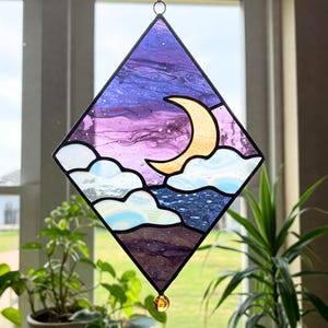 May include: A diamond-shaped stained glass window hanging with a crescent moon and clouds against a purple and blue sky.