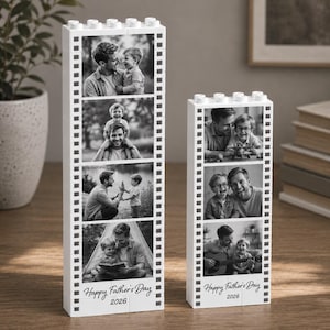 Peut inclure: Deux présentoirs photo blancs en forme de blocs, un grand et un petit, chacun contenant des photos en noir et blanc d'un père et d'un enfant. Le texte "Happy Father's Day 2026" est imprimé en bas de chaque présentoir.