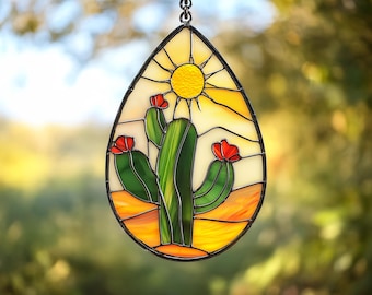 May include: A stained glass suncatcher featuring a green cactus with red flowers and a yellow sun against a white background.