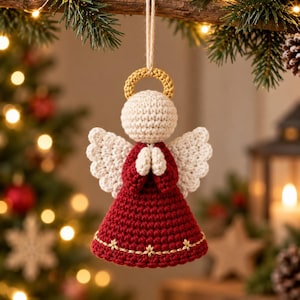 May include: A crocheted angel ornament featuring a round cream-colored head, a gold halo, and a deep red dress with gold embroidered star details. The angel has cream-colored wings and hands pressed together in prayer, suspended by a jute twine loop.