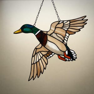 Könnte beinhalten: Ein Buntglasfenster, das an einer Kette hängt und einen fliegenden Stockenten-Erpel zeigt. Der Erpel ist braun, grün und weiß mit einem roten Schnabel und schwarz-weißen Schwanzfedern.