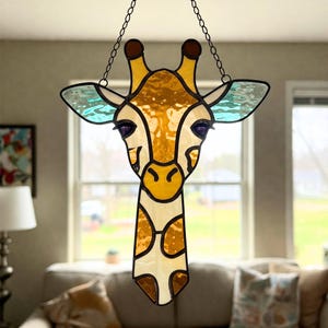 May include: A stained glass giraffe head with a light brown body, a yellow face, and blue ears. The giraffe is hanging from a black chain.