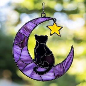 Op de afbeelding: Een zonvanger van gekleurd glas met een zwarte kat die op een paarse halve maan zit met een gele ster erboven.