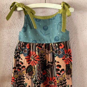 May include: A sleeveless dress with green straps and a floral print. The top of the dress is a light blue fabric with a white polka dot pattern. The bottom of the dress is a pink and brown fabric with a colorful floral print.