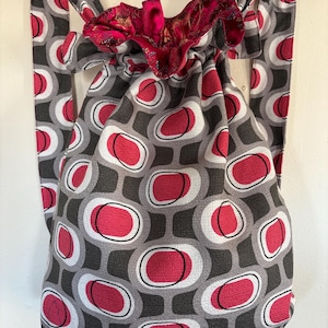 May include: A gray and pink drawstring backpack with a geometric pattern of circles. The backpack has a pink lining and is made of a soft, textured fabric.