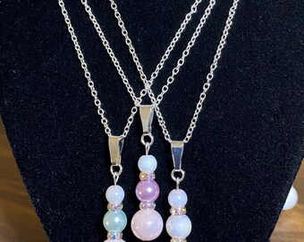 Puede incluir: Tres collares de cadena plateada con colgantes de cuentas superpuestas en rosa, azul y blanco.