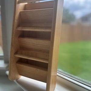 May include: A light-colored wooden desk organizer with a ladder-like design. It features multiple shelves for storing mail, documents, or small items. The organizer is made of natural wood and has a handle at the top.