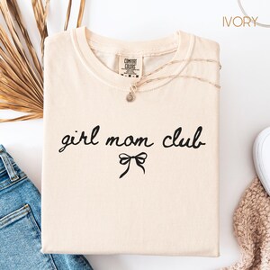 Peut inclure: T-shirt ivoire avec le texte "girl mom club" en &eacute;criture noire avec un n&oelig;ud noir en dessous.