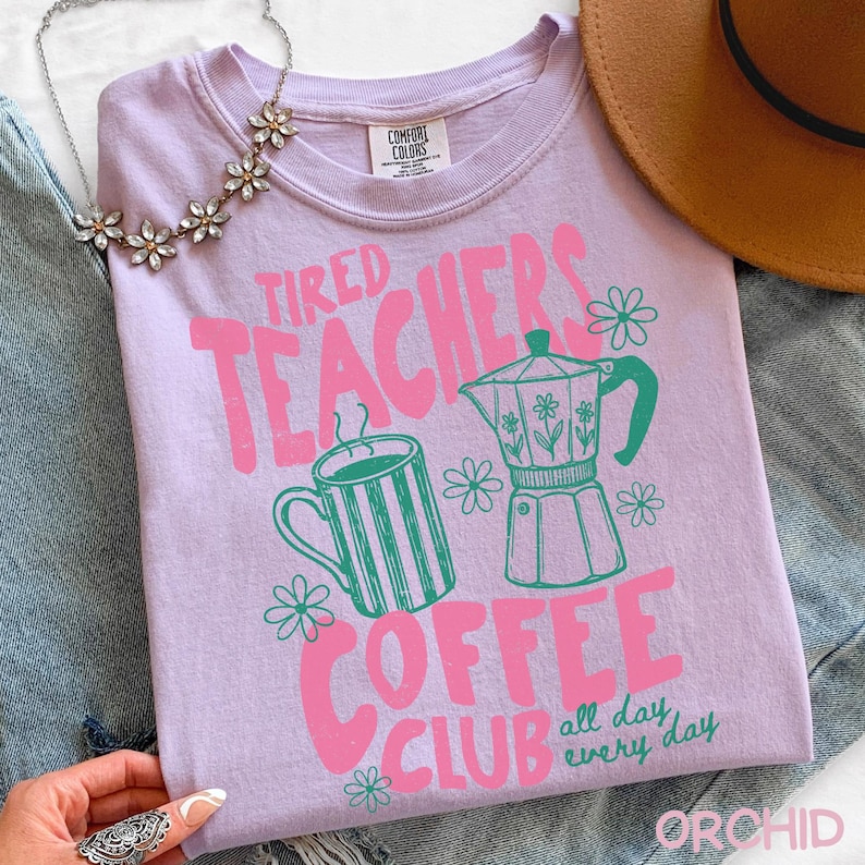 May include: A light purple Comfort Colors t-shirt with a pink and green graphic. The graphic says "Tired Teachers Coffee Club" with images of a coffee mug and a coffee pot. The words "all day every day" are also included.