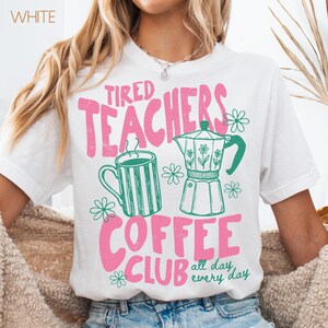May include: White t-shirt with a pink and green graphic. The graphic reads "Tired Teachers Coffee Club" with images of a coffee mug, a coffee pot, and flowers. The phrase "all day every day" is also included.