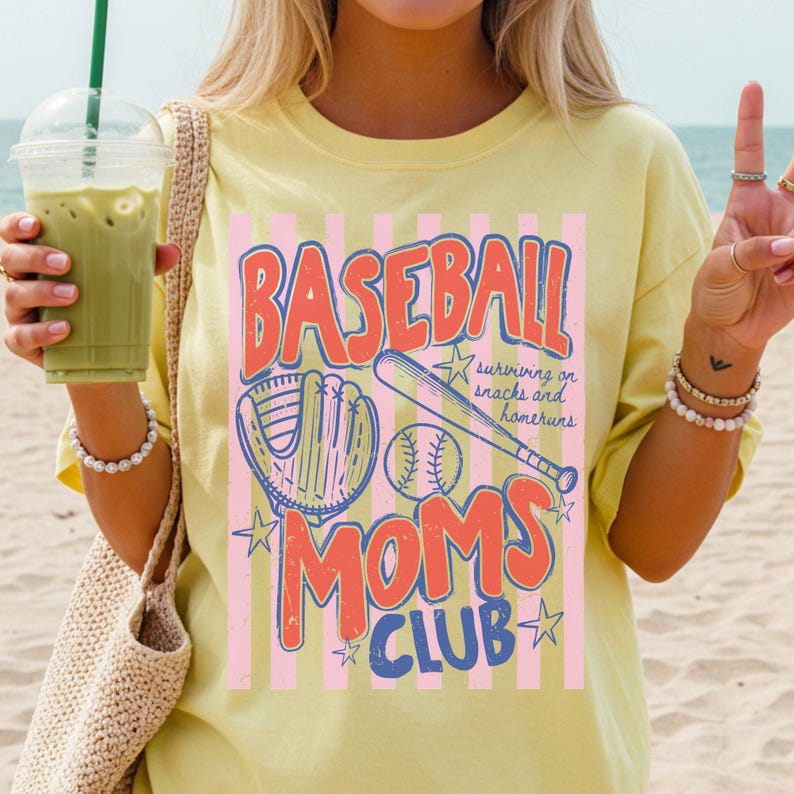 Op de afbeelding: Lichtgeel T-shirt met een honkbalthema. Het ontwerp bevat de woorden "BASEBALL MOMS CLUB" in rood en blauw, samen met honkbaluitrusting. Het shirt heeft een losse pasvorm.