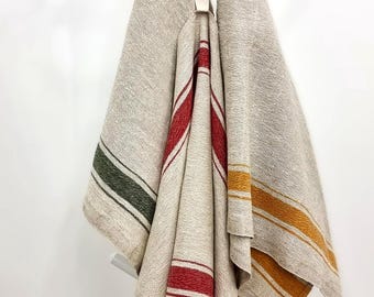May include: Three textured beige kitchen towels hanging from a white hook. Each towel features distinct vertical stripes in different colors: one with dark green stripes, one with bright red stripes, and one with golden yellow stripes.