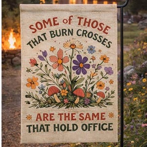 Może przedstawiać: Flaga ogrodowa z napisem "SOME OF THOSE THAT BURN CROSSES ARE THE SAME THAT HOLD OFFICE" w rustykalnej czcionce. Flaga przedstawia kolorowe kwiaty i grzyby. Flaga jest wyświetlana na zewnątrz.