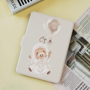 May include: A light beige tablet case with a Halloween-themed illustration. The design features a baby pumpkin wearing a bonnet and a pacifier, with a balloon and ghosts. A small spider is also present.