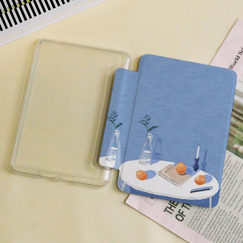 May include: A clear, protective tablet case next to a blue tablet cover with a painted illustration. The illustration depicts a white table with oranges, a candle, and vases with plants. The text "THE OF T" is visible.