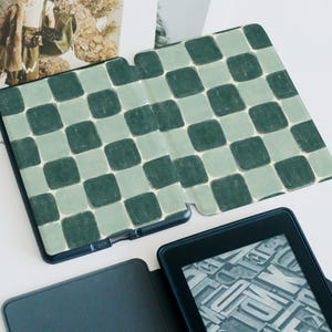 May include: A green and white checkered pattern e-reader case with a black e-reader inside. The e-reader is displaying a page of text.