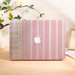 Op de afbeelding: Een harde laptophoes met een verticaal gestreept patroon in roze en wit aan de rechterkant, een decoratieve rand van kant en bloemmotieven, en een ruitjesgedeelte aan de linkerkant, in het midden voorzien van een wit Apple-logo.