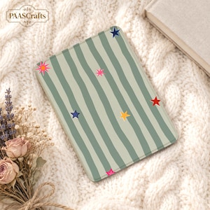 May include: A rectangular e-reader cover featuring a light sage green background with vertical wavy dark green stripes. The cover is decorated with scattered multi-coloured stars in shades of pink, yellow, red, and dark blue. The logo PAASCRAFTS is visible.