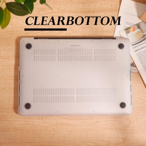 May include: A clear laptop case with the text "CLEARBOTTOM" above it. The case is designed for a MacBook Pro and has ventilation slots and four black rubber feet. The case is on a light brown wooden surface.
