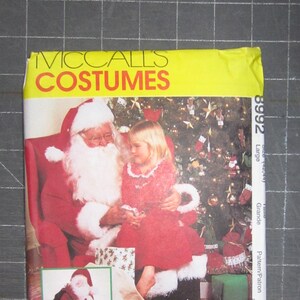 May include: McCall's Costumes sewing pattern for a Santa Claus and a girl's Christmas dress. The pattern number is 8992. The image shows a Santa Claus sitting with a girl wearing a red dress and a white fur trim. The girl is holding a small gift.