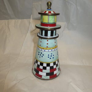 May include: A decorative lighthouse-shaped object featuring a brass-colored finial and horizontal tiers. The exterior is painted with colorful patterns including red, white, and black checkered sections, light blue bands with dots, and yellow stripes.