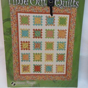 May include: A green and orange book cover with the title "Time Out Quilts" and a black cat clock with a bow tie. The book cover features a quilt design with a variety of colorful squares.
