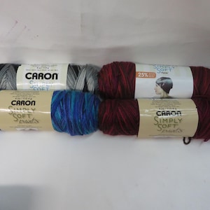 May include: Four skeins of Caron Simply Soft yarn in various colors. The skeins are labeled "Caron Simply Soft Prints" and "Caron Simply Soft".