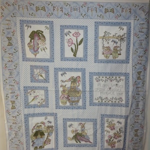 May include: A white fabric panel with a blue and white checkered pattern. The panel features a variety of images, including bunnies, flowers, and butterflies. The text "Plant Smiles Grow Goodies Harvest Love" is printed on the panel.