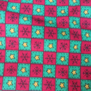 May include: A festive fabric with a repeating pattern of red and green squares. Each square contains a yellow star or a black snowflake design. The fabric is likely for holiday-themed crafts or decor.