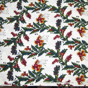 May include: White fabric with a repeating pattern of green, red, and yellow floral designs. The fabric has the text "Guaranteed Cotton" printed on the bottom.