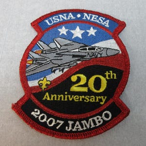 May include: A red, white, and blue embroidered patch with a fighter jet, three stars, and the text "USNA NESA 20th Anniversary 2007 JAMBO".