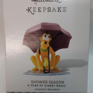May include: Hallmark Keepsake ornament featuring a cartoon dog holding an umbrella over a small yellow chick. The ornament is titled "Shower Season A Year of Disney Magic".