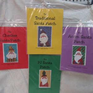 May include: Four colorful Santa Claus patch kits in plastic packaging. The kits are titled "The Checker Santa Patch", "The Traditional Santa Patch", "The Acorn Santa Patch", and "The PJ Santa Patch". Each kit features a Santa Claus design.