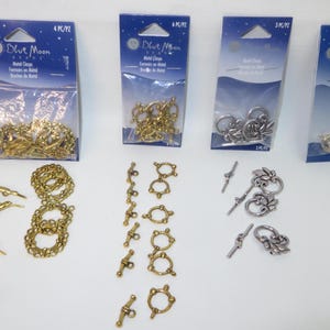 May include: An assortment of metal clasps and jewelry findings in gold and silver tones. The image includes various styles of clasps, including toggle clasps, lobster clasps, and decorative connectors, perfect for jewelry making and crafting.