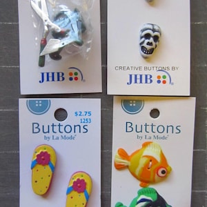 May include: Four cards with buttons on them. The top left card has a gardener's set with a pair of scissors and a watering can. The top right card has two skull buttons. The bottom left card has two hand-painted flip-flop buttons. The bottom right card has two fish buttons, one orange and one green.