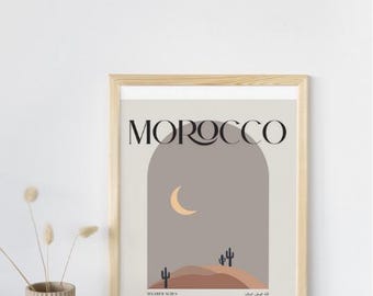 Peut inclure: Une affiche encadrée avec le mot "MOROCCO" en lettres noires. L'œuvre représente un paysage désertique avec un croissant de lune, des cactus et du texte en arabe. Le cadre est en bois clair.