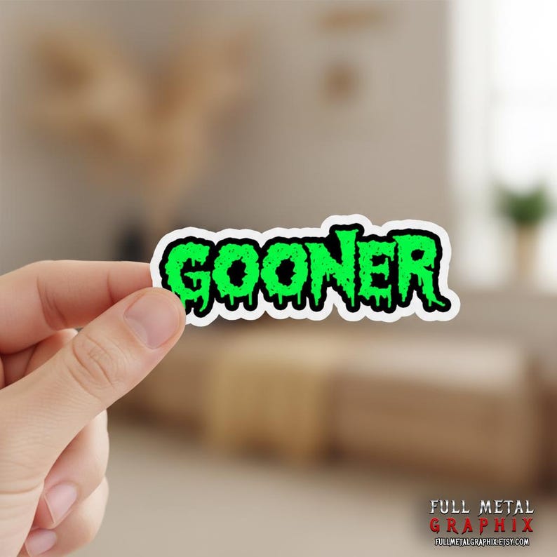 May include: A sticker with the word "GOONER" in dripping green letters with a black outline. The sticker is held by a person's hand. The sticker has a white border. The bottom right corner of the sticker has the text "FULL METAL GRAPHIX".