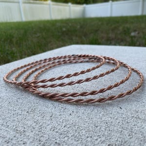 May include: A set of three circular rings crafted from twisted copper wire. Each ring features a continuous, spiraled texture formed by two strands of metallic copper wire wound together to create a uniform, rounded, and flexible hoop design.