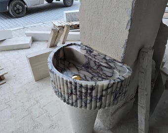May include: A white marble sink with a fluted edge and a pink and purple marbling pattern. The sink is mounted on a white pedestal.