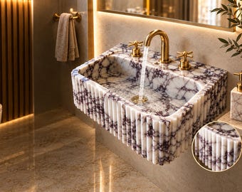 May include: A rectangular wall-mounted bathroom sink crafted from white marble with deep purple veining. The exterior features a vertical fluted design. It includes a gold-toned faucet with two cross-handle knobs and a matching drain.
