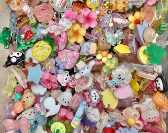 May include: A collection of colorful resin charms in various shapes, including flowers, animals, bows, and stars. The charms are in shades of pink, yellow, blue, and green, with some featuring glitter and other decorative elements. These are ideal for crafting and jewelry making.