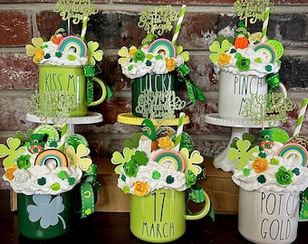 Peut inclure: Cinq tasses décorées avec des accents verts, blancs et dorés. Les tasses sont surmontées de crème fouettée, de pépites et d'autres décorations festives. Les tasses sont étiquetées "Kiss Me I'm Irish", "Lucky", "Pinch Me", "17 March" et "Pot O' Gold".