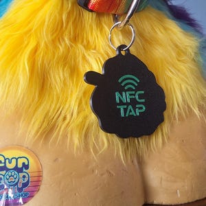 May include: A black, cloud-shaped NFC tag with green text reading NFC TAP and a Wi-Fi symbol, attached to a rainbow-colored faux fur collar. A circular sticker with the text Fur Pop and a paw print icon is visible on the tan mannequin base.