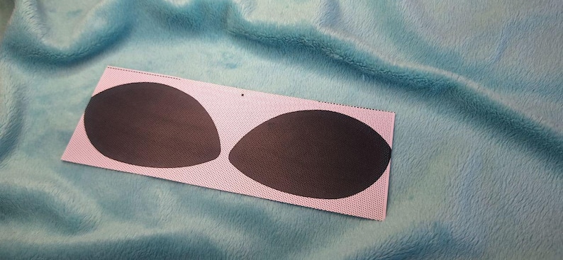 Puede incluir: Una tela rectangular rosa con dos almohadillas ovaladas de color marr&oacute;n oscuro. La tela tiene un patr&oacute;n de puntos y est&aacute; colocada sobre un fondo azul texturizado. Las almohadillas son lisas y opacas.