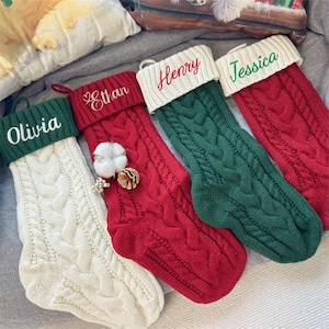 Peut inclure: Quatre chaussettes de Noël personnalisées avec des noms brodés sur le revers. Les chaussettes sont en tissu tricoté avec un motif en tricot torsadé. Les chaussettes sont en rouge, vert et blanc.