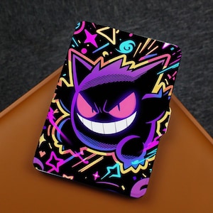 Puede incluir: Una funda protectora rectangular con un gráfico vibrante de un personaje Gengar morado con ojos rosas brillantes y una amplia sonrisa blanca. El fondo es negro y está decorado con estrellas, espirales y formas geométricas de estilo neón.