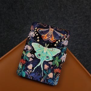 May include: A black and green notebook cover featuring a colourful illustration of two moths and flowers. The moths are a luna moth and a saturniid moth.