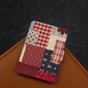Op de afbeelding: Een patchwork-stijl hoesje met diverse patronen en kleuren. Het heeft rode harten, ruitjes, bloemenmotieven en strikken. De hoes, waarschijnlijk voor een tablet of e-reader, heeft een magnetische sluiting.